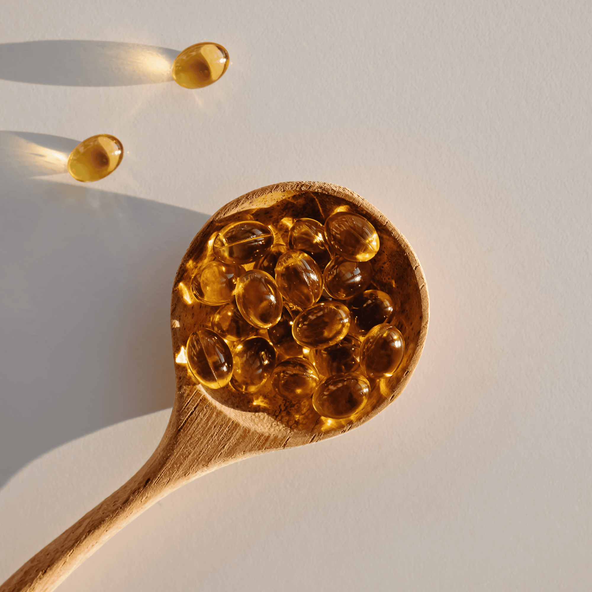 Can Supplements Cause Acne? Softgel supplement capsules in a wooden spoon on a beige background.